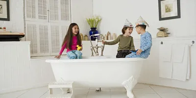 Trois enfants jouent sur le rebord d’une baignoire dans une salle de bain propre. 