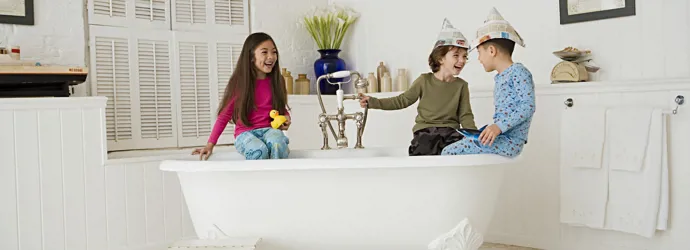 Trois enfants jouent sur le rebord d’une baignoire dans une salle de bain propre. 