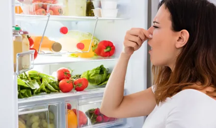 Femme qui se bouche le nez devant un frigo ouvert rempli d'aliments variés.