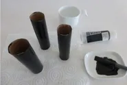 Trois tubes en carton peints en noir, un pinceau, une assiette avec de la peinture noire et un tube de peinture noire.