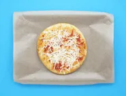 Une pizza à la sauce tomate et au fromage râpé sur une plaque couverte de papier cuisson.