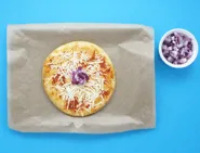 Un bol d'oignons émincés et une pizza margherita avec des oignons au centre sur une plaque couverte de papier cuisson.