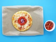 Un bol de tomates coupées en deux et une pizza margherita aux oignons et tomates sur une plaque de cuisson couverte.