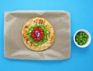 Des poivrons verts émincés et une pizza margherita aux oignons, tomates et poivrons sur une plaque de cuisson couverte.