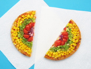 La pizza arc-en-ciel finie aux oignons, tomates, poivrons verts et maïs qui a été coupée en deux sur de l'essuie-tout.