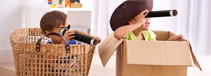 Deux garçons habillés en costumes de pirate qui jouent dans des boîtes en carton et tiennent des longue-vues en carton.