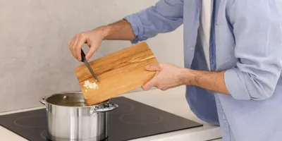Un homme ajoute de l'ail haché dans une casserole sur une cuisinière à induction.