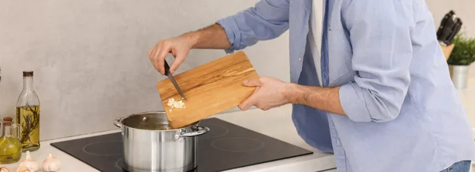 Un homme ajoute de l'ail haché dans une casserole sur une cuisinière à induction.