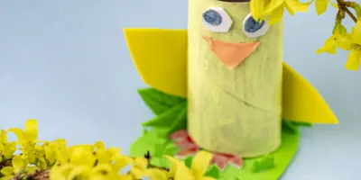 Un animal en carton fait d'un rouleau d'essuie-tout : un poussin jaune avec un bec orange et de grands yeux dessinés.