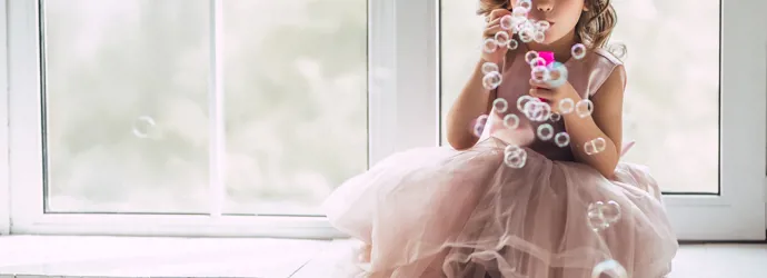 Une petite fille en costume de princesse rose fait des bulles