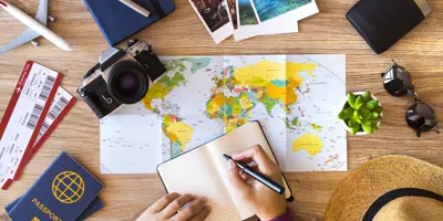 Une main tient un livre et un stylo sur un bureau, sur lequel se trouve une variété d'objets associés aux vacances d'été