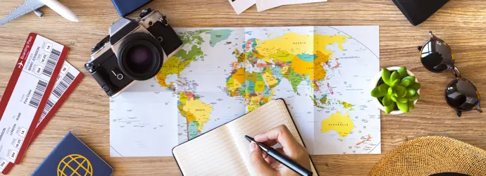 Une main tient un livre et un stylo sur un bureau, sur lequel se trouve une variété d'objets associés aux vacances d'été
