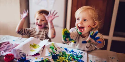 Twee kinderen spelen met hun rommelige handen met een kunstenaarspalet en blauwe verf