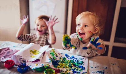 Twee kinderen spelen met hun rommelige handen met een kunstenaarspalet en blauwe verf