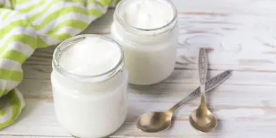 Twee jampotten met zelfgemaakte yoghurt staan op een houten tafel