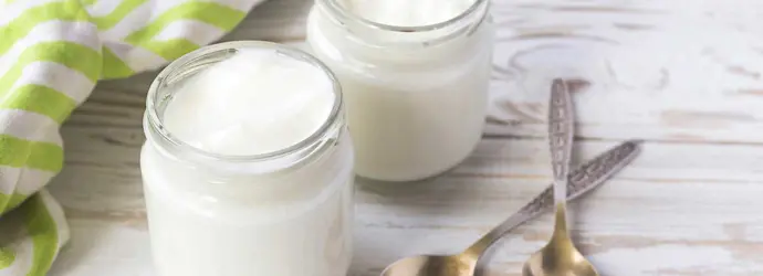 Twee jampotten met zelfgemaakte yoghurt staan op een houten tafel