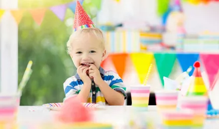 Kind viert verjaardag met verjaardagshoedje op aan een versierde verjaardagstafel
