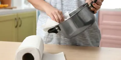 Een persoon naast het aanrecht en maakt een pot schoon met een vel keukenpapier
