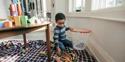 enfant de 3 ans ramassant des jouets et les mettant dans un panier