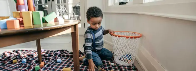enfant de 3 ans ramassant des jouets et les mettant dans un panier
