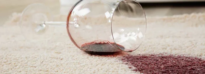 Verre à vin renversé sur un tapis créant une tache de vin