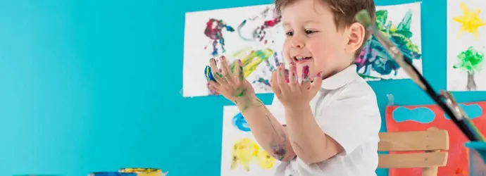 Een kind zit aan tafel en verft met zijn vingers
