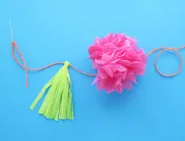 Une fleur en papier essuie-tout rose, et un pompon vert clair attachés ensemble avec une ficelle rouge.