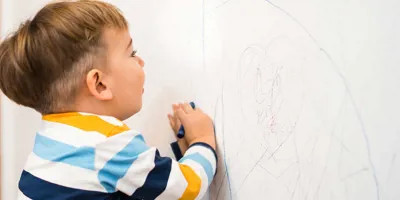 Un bébé dessine sur un papier peint propre avec des crayons