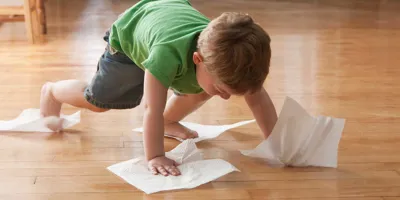 Un enfant nettoie le sol avec des essuie-tout