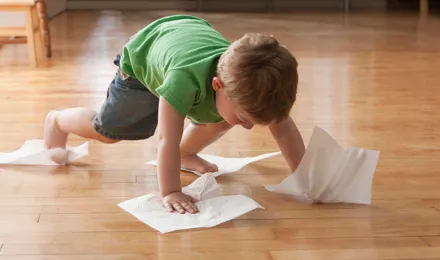 Un enfant nettoie le sol avec des essuie-tout