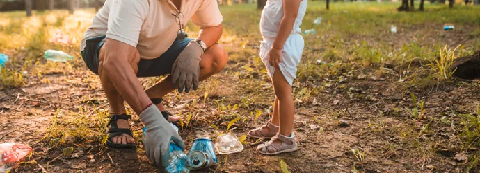 Un grand-père apprend à un enfant à ramasser les déchets dans un parc ensoleillé.