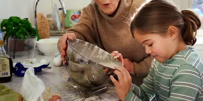 Petite fille cuisinant avec sa grand-mère dans une cuisine en désordre.