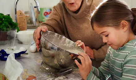 Petite fille cuisinant avec sa grand-mère dans une cuisine en désordre.