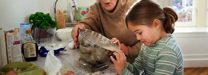 Petite fille cuisinant avec sa grand-mère dans une cuisine en désordre.