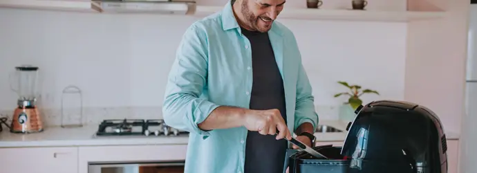 Un homme souriant utilise des pinces pour remuer le contenu d'un air fryer.