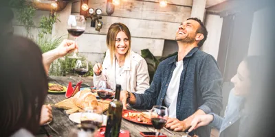 Un groupe d'amis souriants, dégustant du vin et de la nourriture autour d'une table lors d'une garden party.