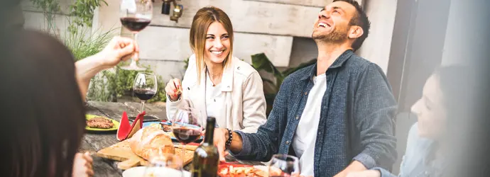 Un groupe d'amis souriants, dégustant du vin et de la nourriture autour d'une table lors d'une garden party.