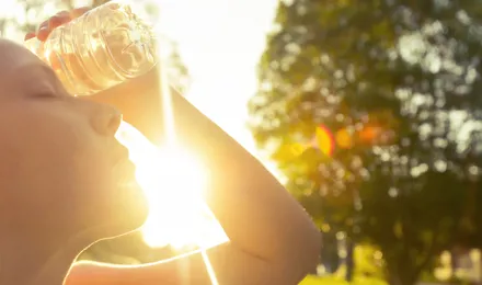 Un enfant est dehors sous le soleil et pose une bouteille d'eau sur son front pour se rafraîchir.