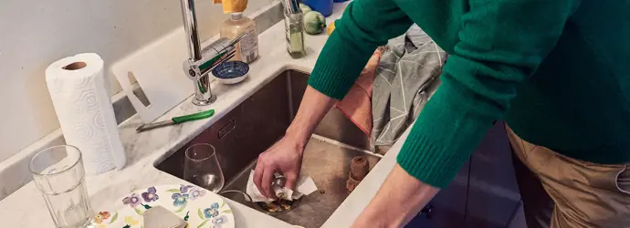 Homme en pull-over vert nettoyant l'évier de la cuisine avec un mouchoir.