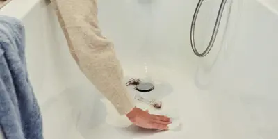 Femme en train d'enlever les cheveux du drain de bain.