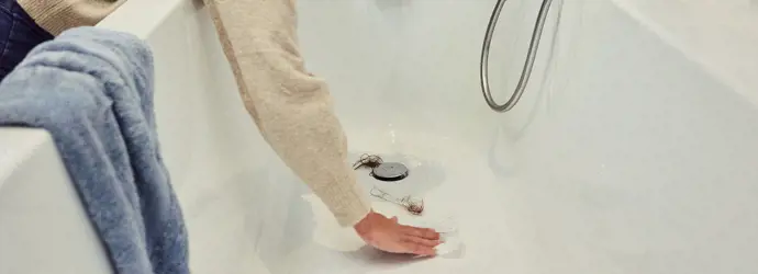 Femme en train d'enlever les cheveux du drain de bain.