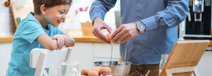 Un homme et un enfant cassent joyeusement des œufs dans un saladier.