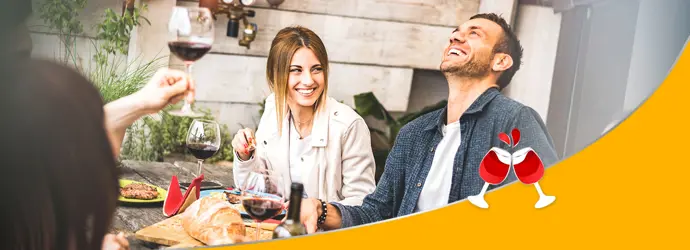Un groupe d'amis souriants, dégustant du vin et de la nourriture autour d'une table lors d'une garden party.