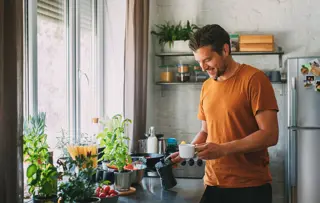 Un homme sourit en préparant un café dans sa cuisine.