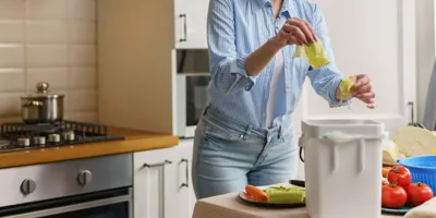 Une femme en chemise bleue épluche des légumes dans un bac à compost.