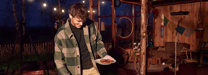 Jeune homme cuisinant sur un barbecue dans le jardin le soir.
