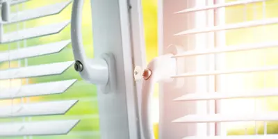 Gros-plan sur une fenêtre entre-ouverte sur laquelle se trouvent des stores blancs.