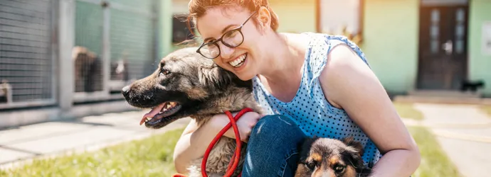 Une jeune femme s'accroupit et prend son chien dans ses bras dans un jardin ensoleillé.