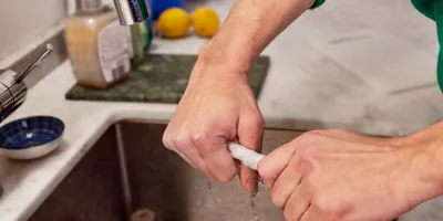 Mains d'une personne portant un pull-over vert nettoyant l'évier de la cuisine en essorant un essuie-tout mouillé.
