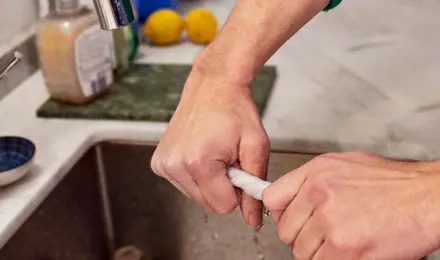 Mains d'une personne portant un pull-over vert nettoyant l'évier de la cuisine en essorant un essuie-tout mouillé.